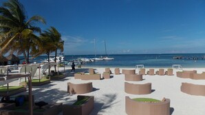 A beach with lounge chairs and palm trees, boats in the water, and a clear sky. - Ocean Spa Hotel – All Inclusive (Cancun)