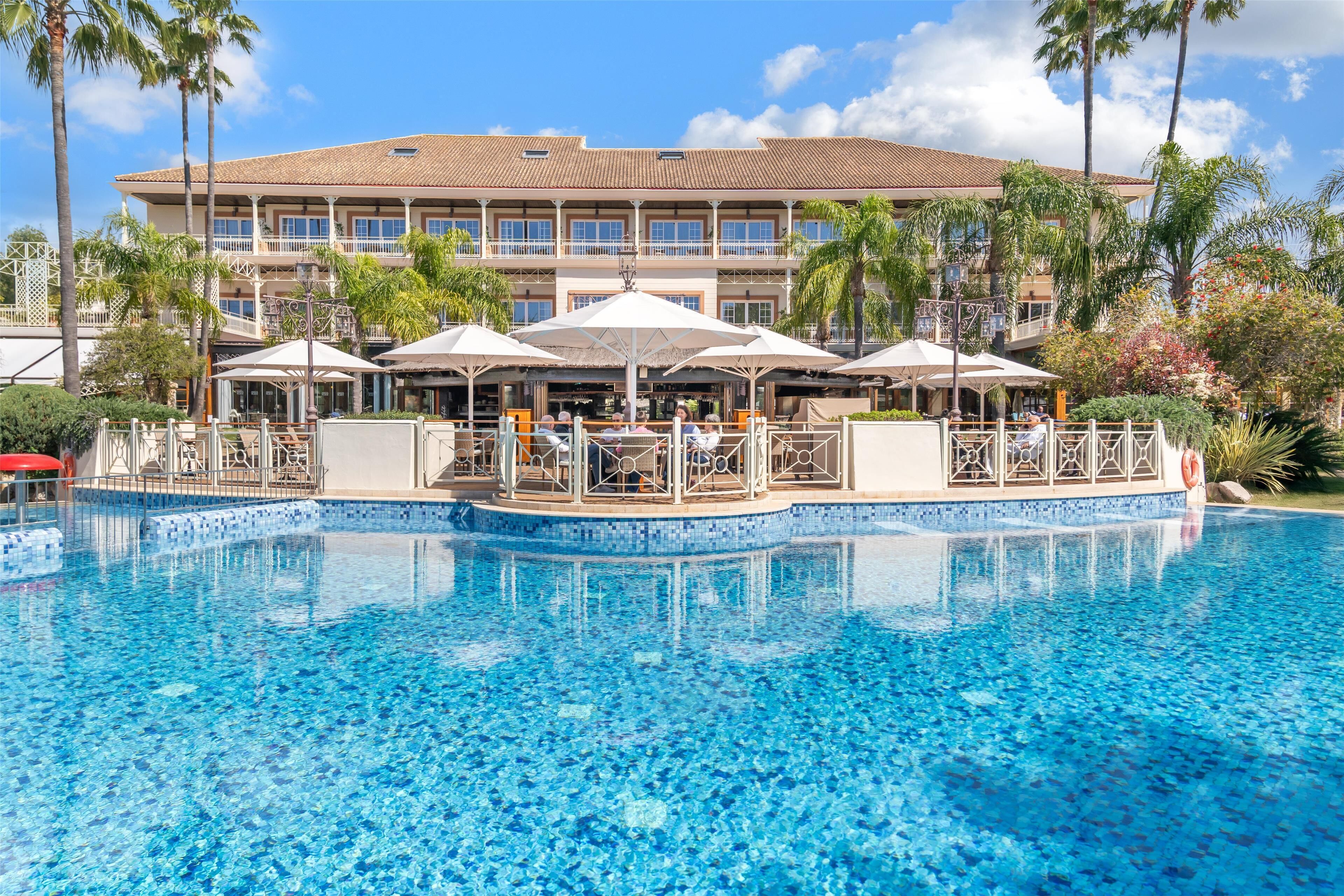 Un hotel con piscina, mobiliario exterior y palmeras.