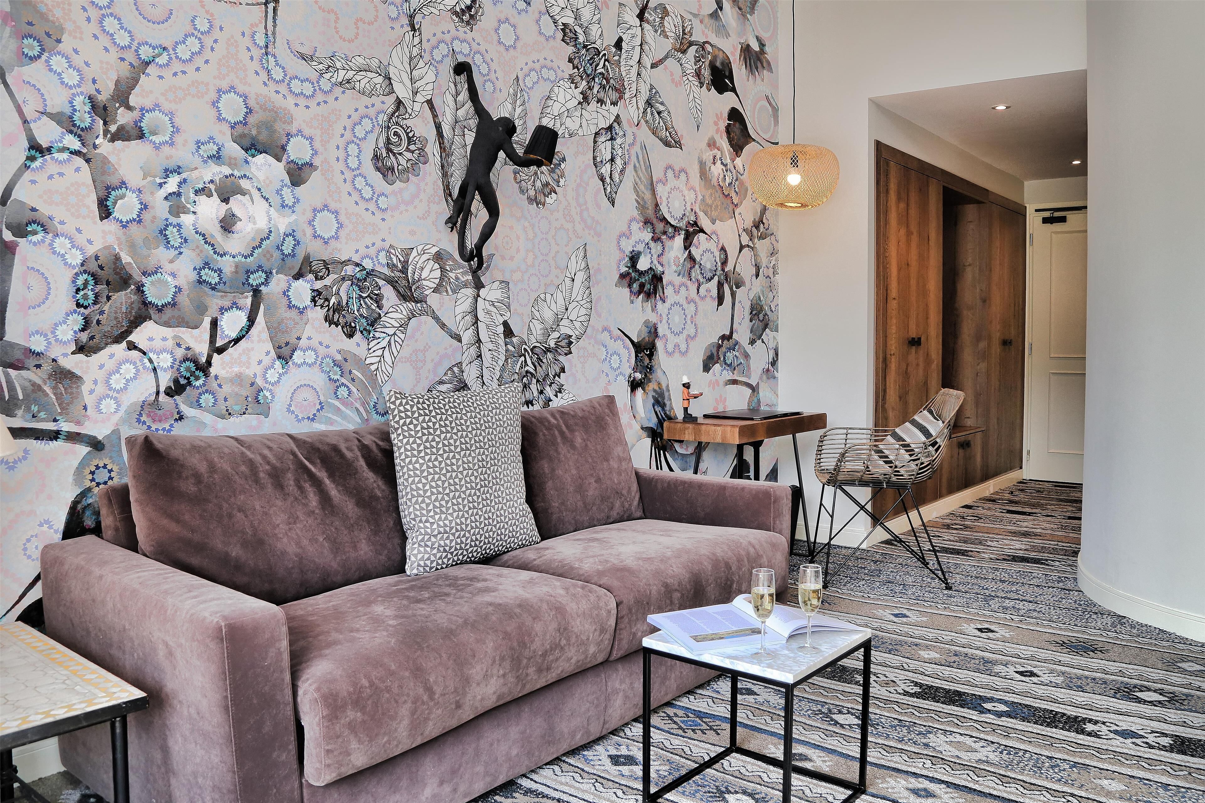 A modern living room with a plush pink sofa, a small coffee table, and a patterned wall mural.