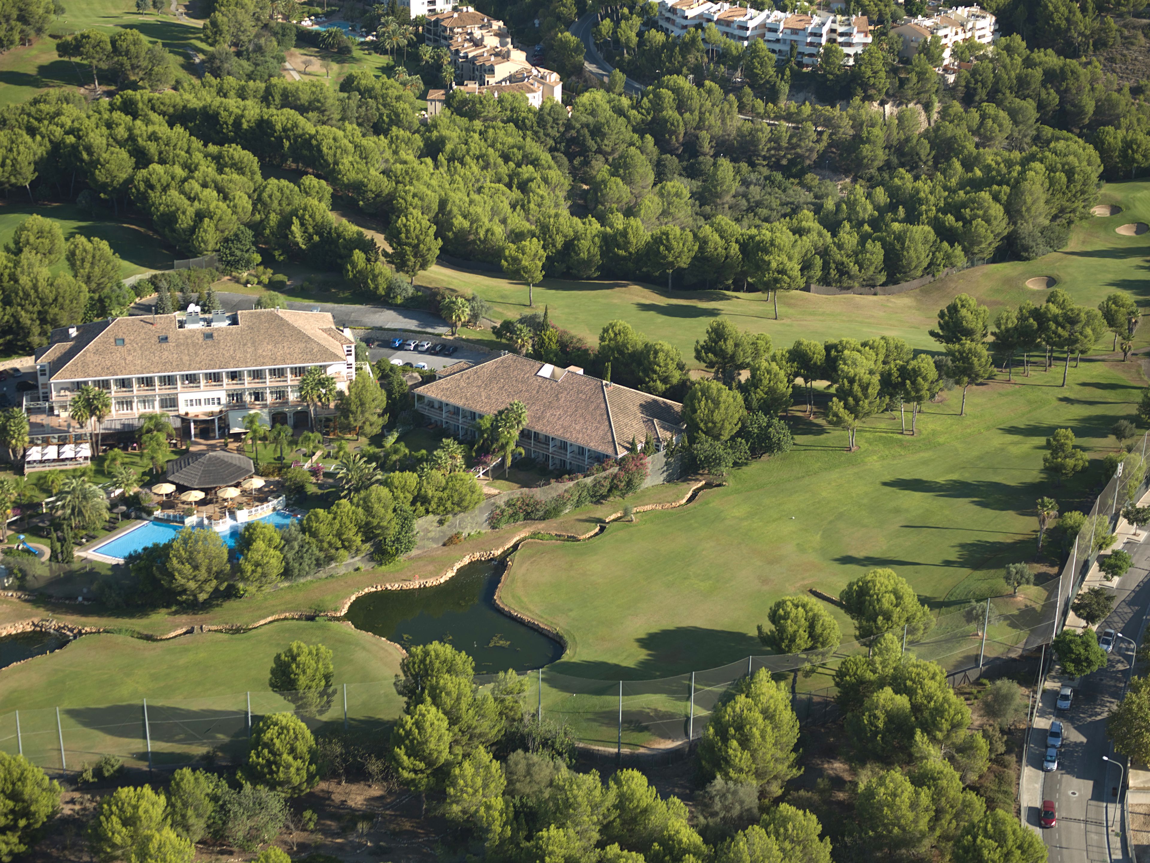 An aerial view of a golf course with a clubhouse, a swimming pool, and surrounding greenery.