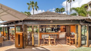 Un restaurante con techo de paja, mesas al aire libre y una zona de bar.