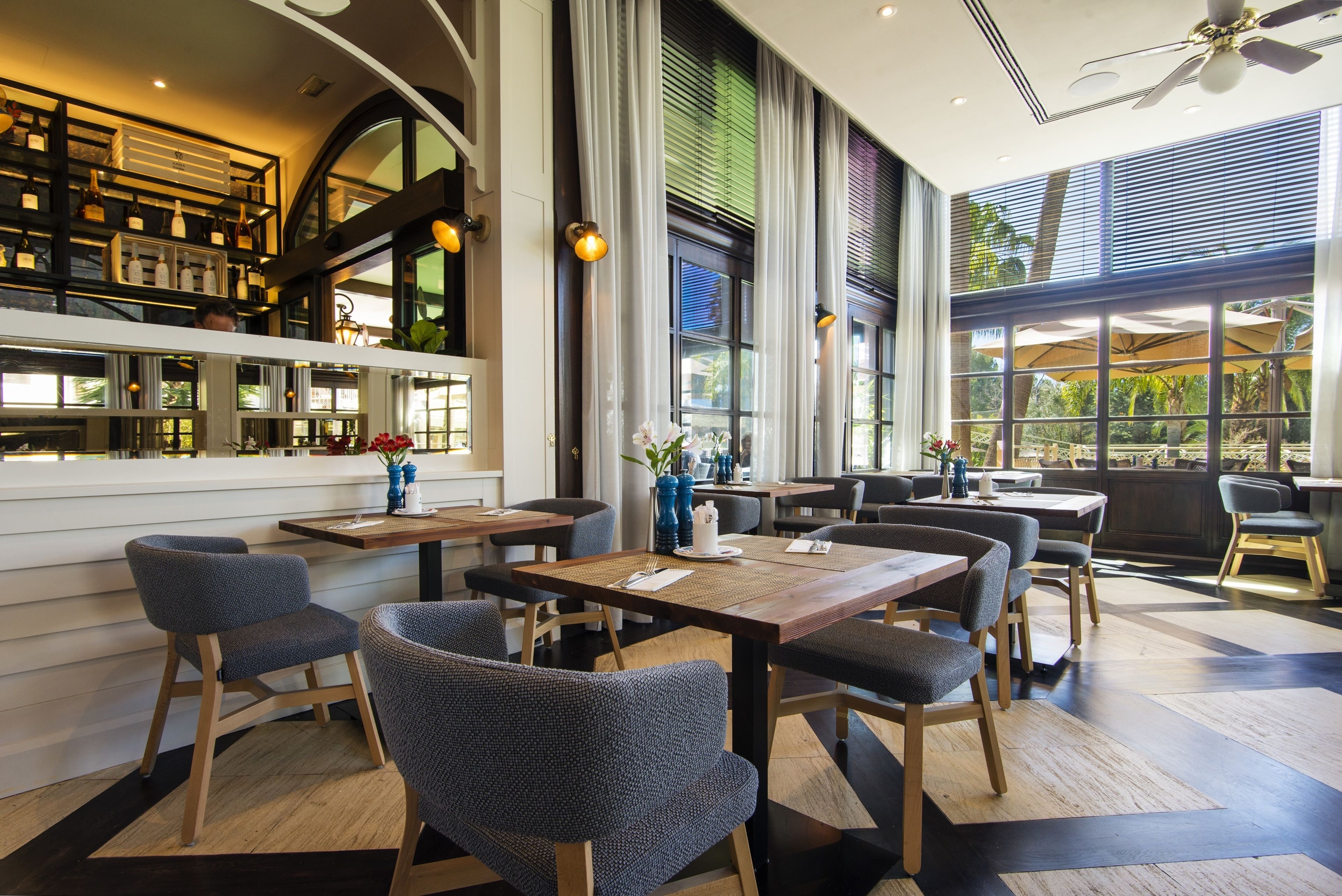 A modern restaurant with high ceilings, large windows, and a variety of seating arrangements.