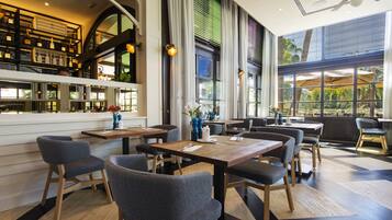 A modern restaurant with high ceilings, large windows, and a variety of seating arrangements.