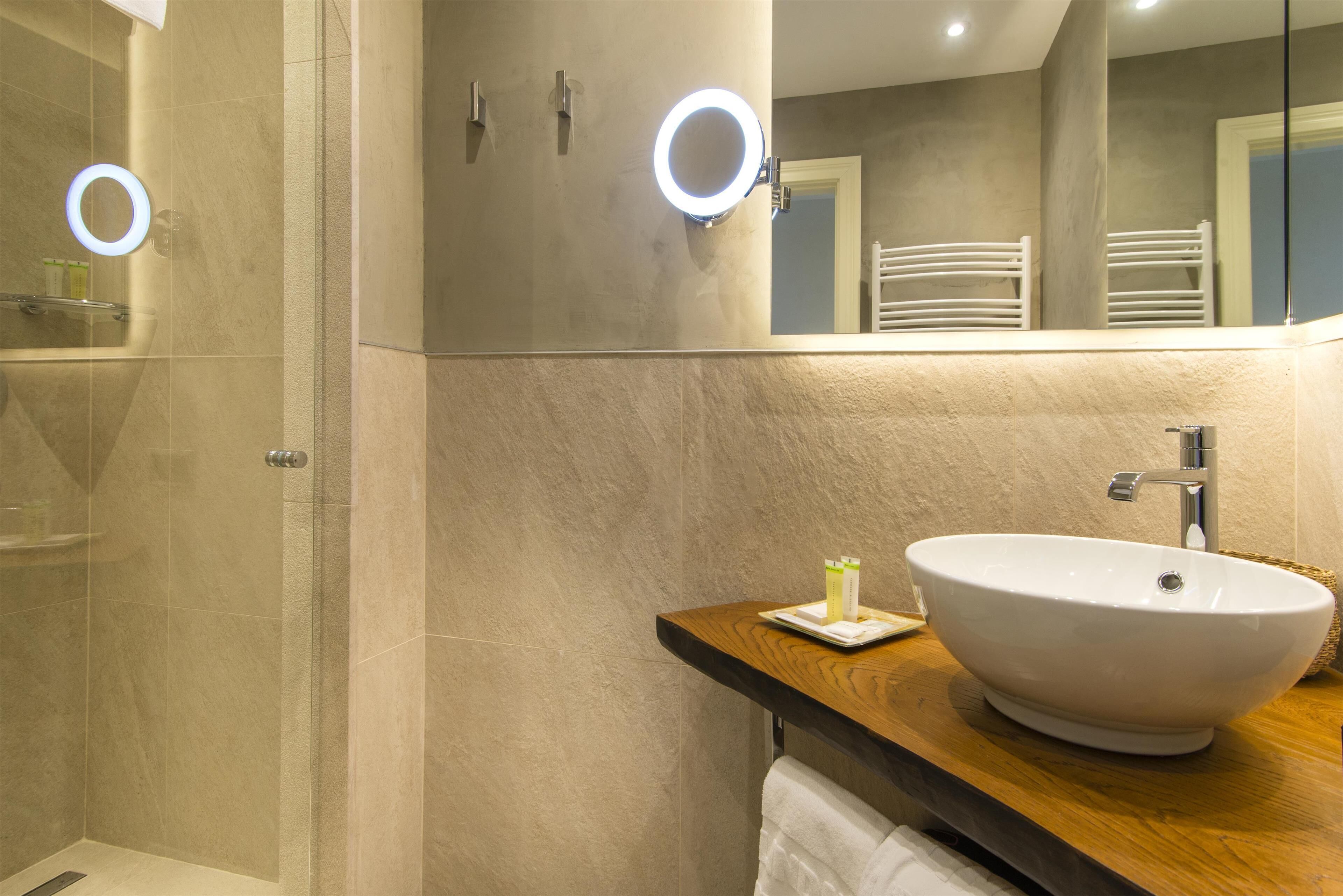 Un baño con un espejo grande, un lavamanos blanco y una zona de ducha.