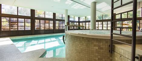 An indoor swimming pool with a hot tub, large windows, and a tiled floor.