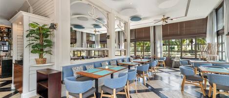 A modern restaurant with high ceilings, large windows, and a mix of seating arrangements including booths and tables.