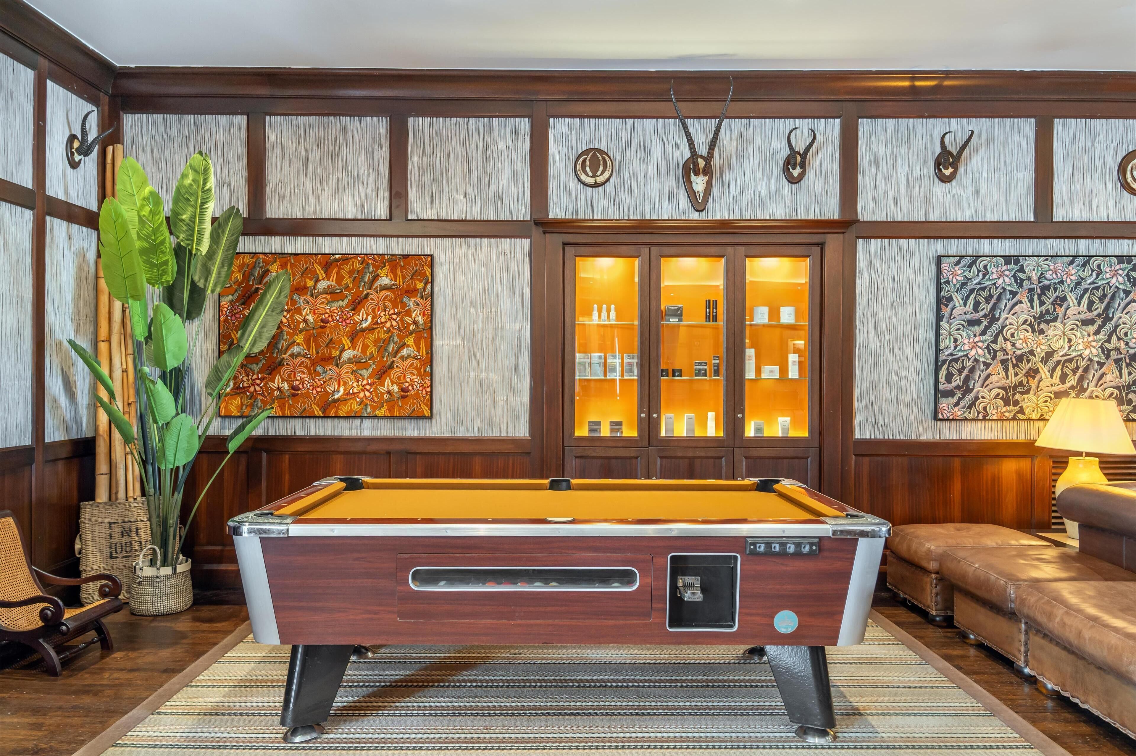 A pool table in a room with wooden paneling, a sofa, and decorative wall art.