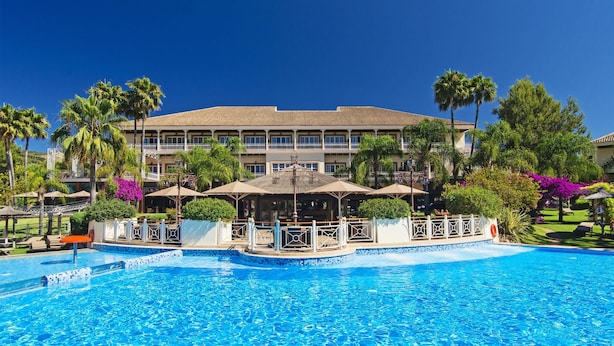 Un hotel con piscina, palmeras y un edificio grande con varios balcones.