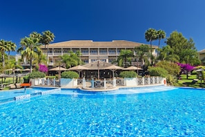 A hotel with a swimming pool, palm trees, and a large building with multiple balconies. - Lindner Hotel Mallorca Portals Nous, part of JdV by Hyatt (Calvia)