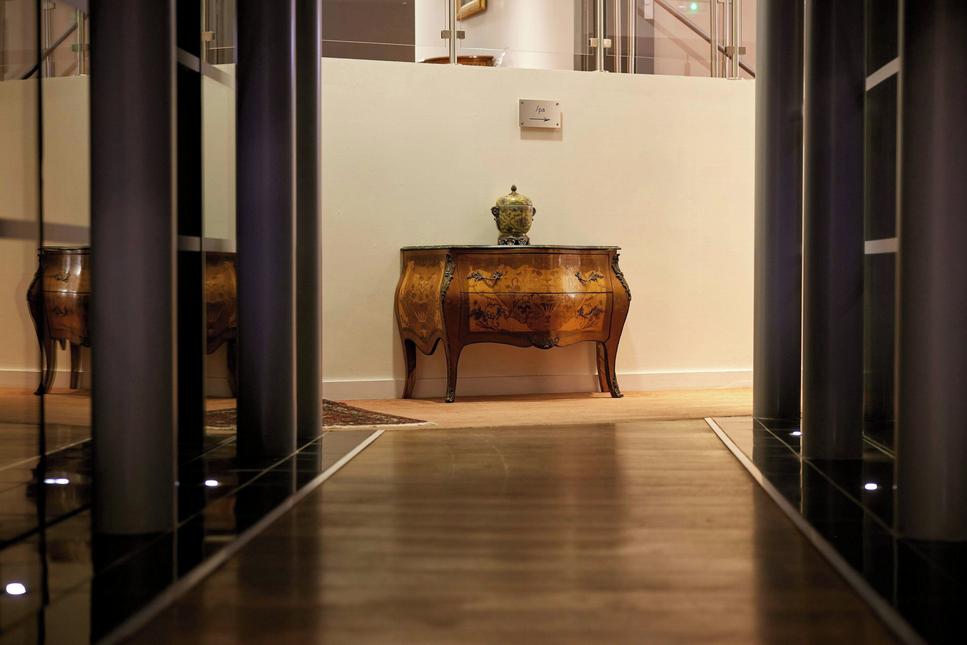 Un plancher en bois poli mène à un coin où se trouve un meuble en bois et un vase décoratif.
