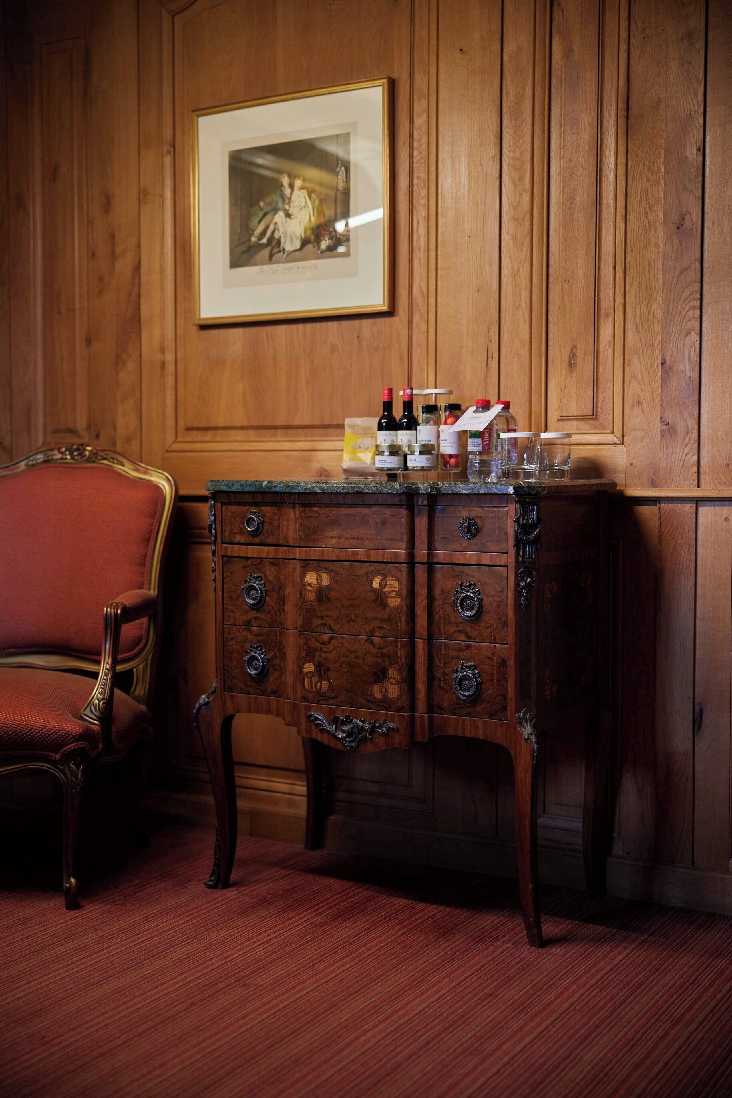 A wooden-paneled room with a vintage-style cabinet, a framed picture on the wall, and a red upholstered chair.