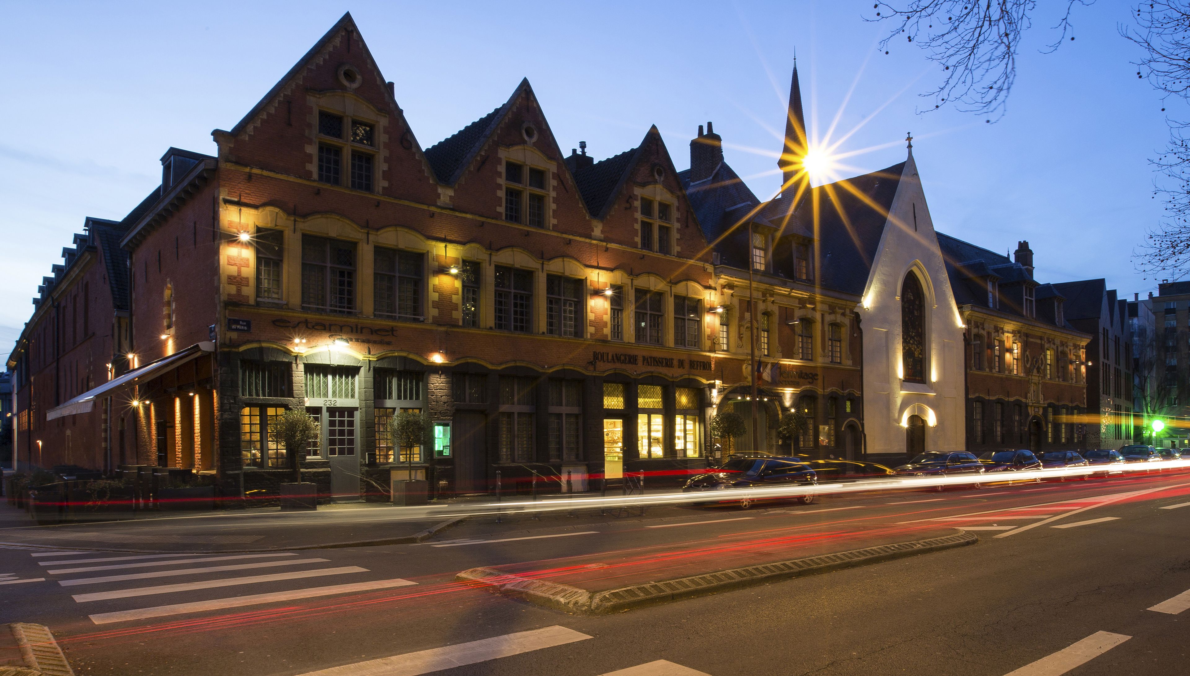 Een historisch gebouw met een opvallende kerktoren, grote ramen en een straatbeeld met auto's.