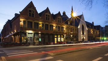 Een historisch gebouw met een opvallende kerktoren, grote ramen en een straatbeeld met auto's.