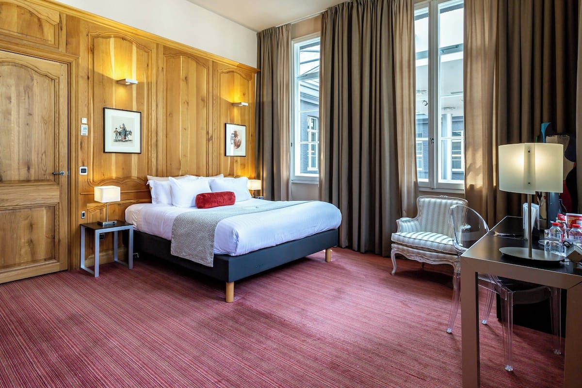Une chambre d’hôtel avec un grand lit, une chaise, un bureau et une fenêtre avec des rideaux.
