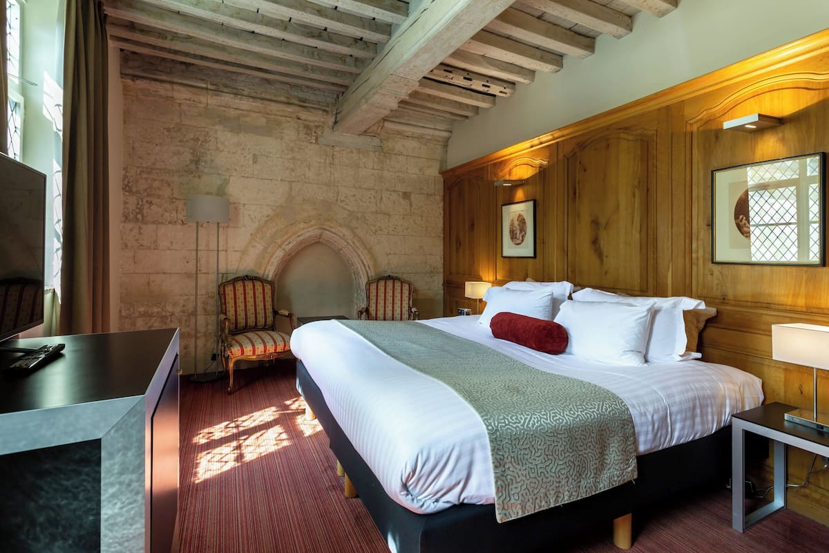 Une chambre d’hôtel avec un grand lit, un bureau, une chaise et un mur en bois orné d’un cadre de tableau.