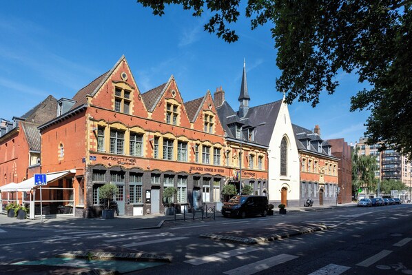 A historic building with a prominent church steeple, a café, and a row of parked cars. - L'Hermitage Gantois, Autograph Collection (Lille)