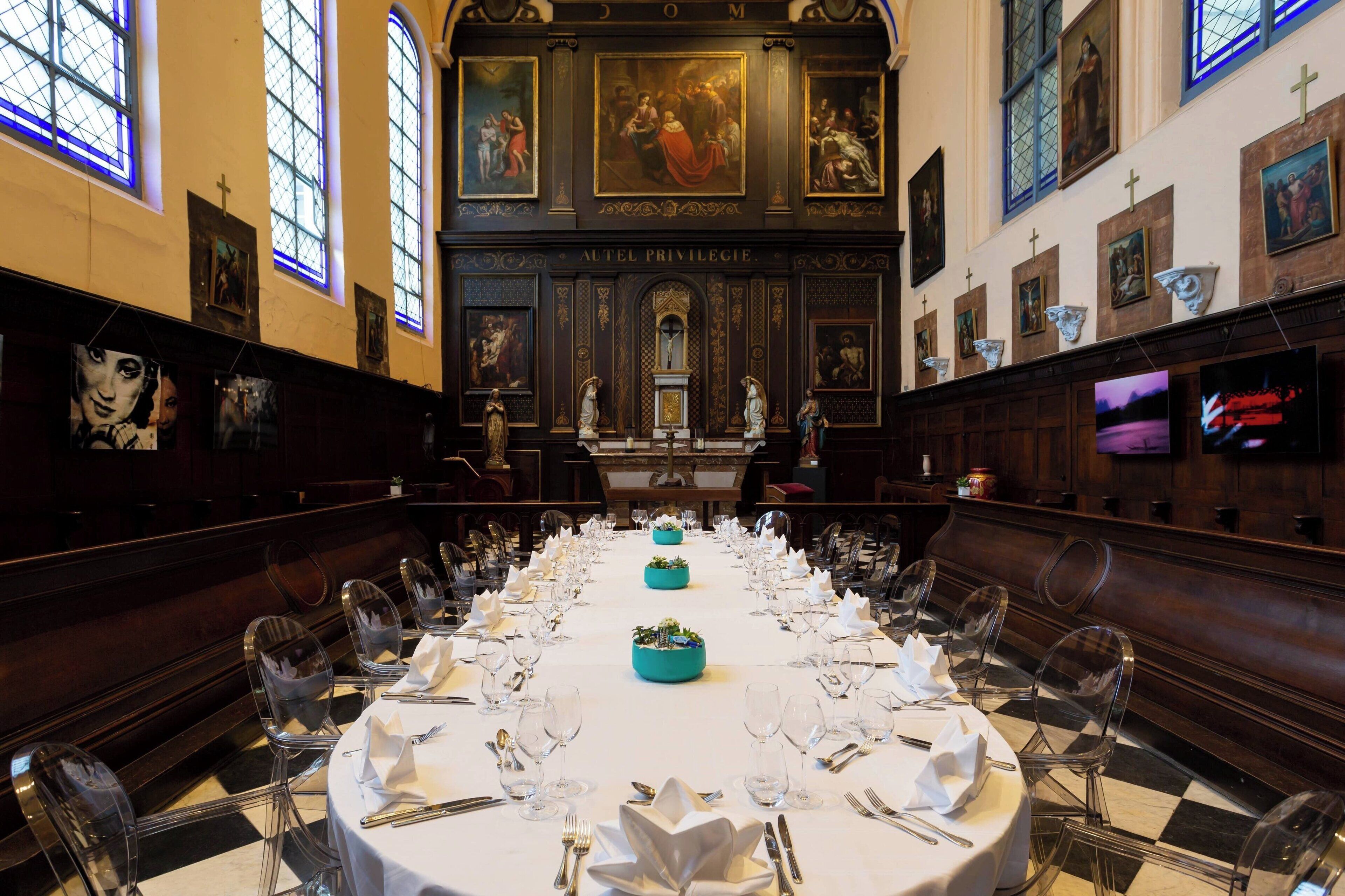 A banquet hall with a long table set for a formal event, flanked by wooden pews and framed artwork on the walls.