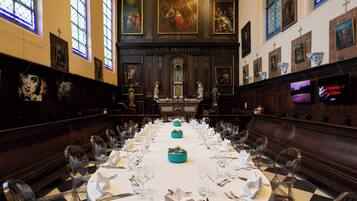 A banquet hall with a long table set for a formal event, flanked by wooden pews and framed artwork on the walls.