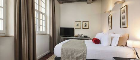 Una habitación de hotel con cama, televisión, mesita de noche y lámpara.