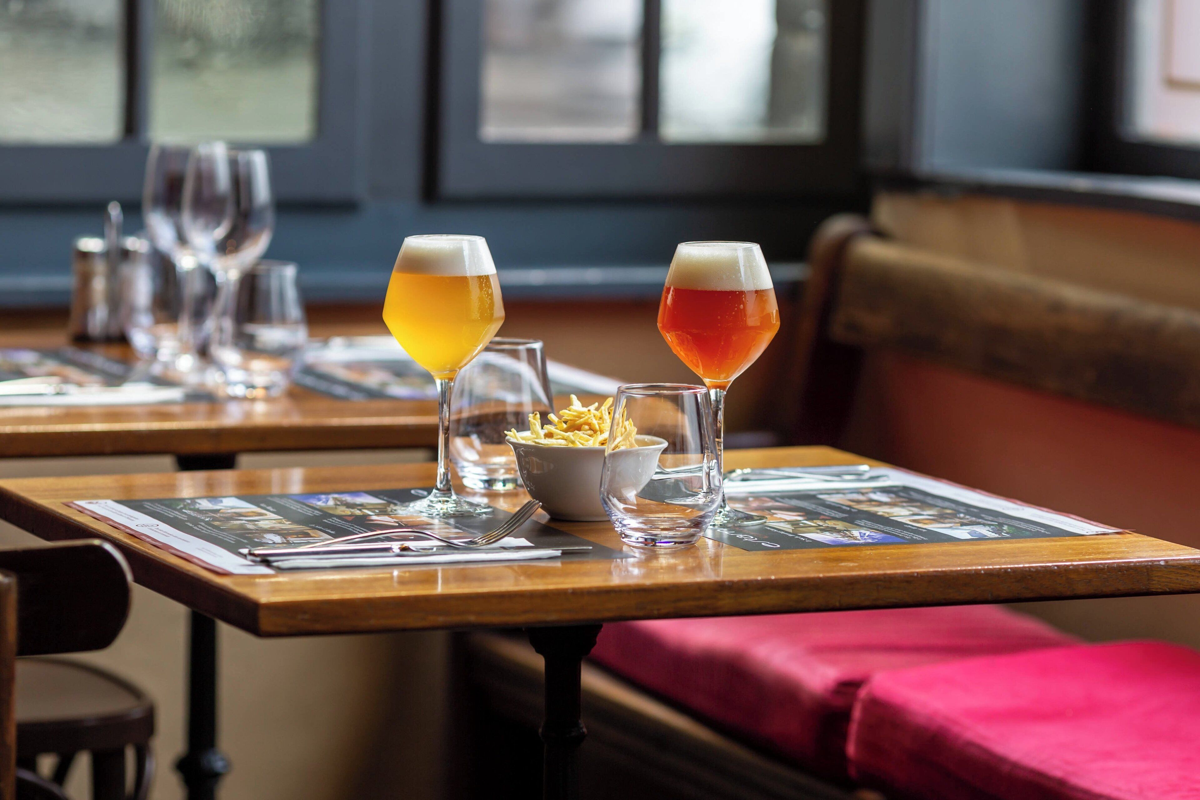 A restaurant setting with tables set for dining, featuring glasses of beer and a bowl of fries.