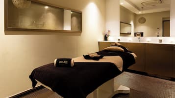 Une salle de spa moderne équipée d’une table de massage, d’un grand miroir et d’un lavabo avec un porte-serviettes.