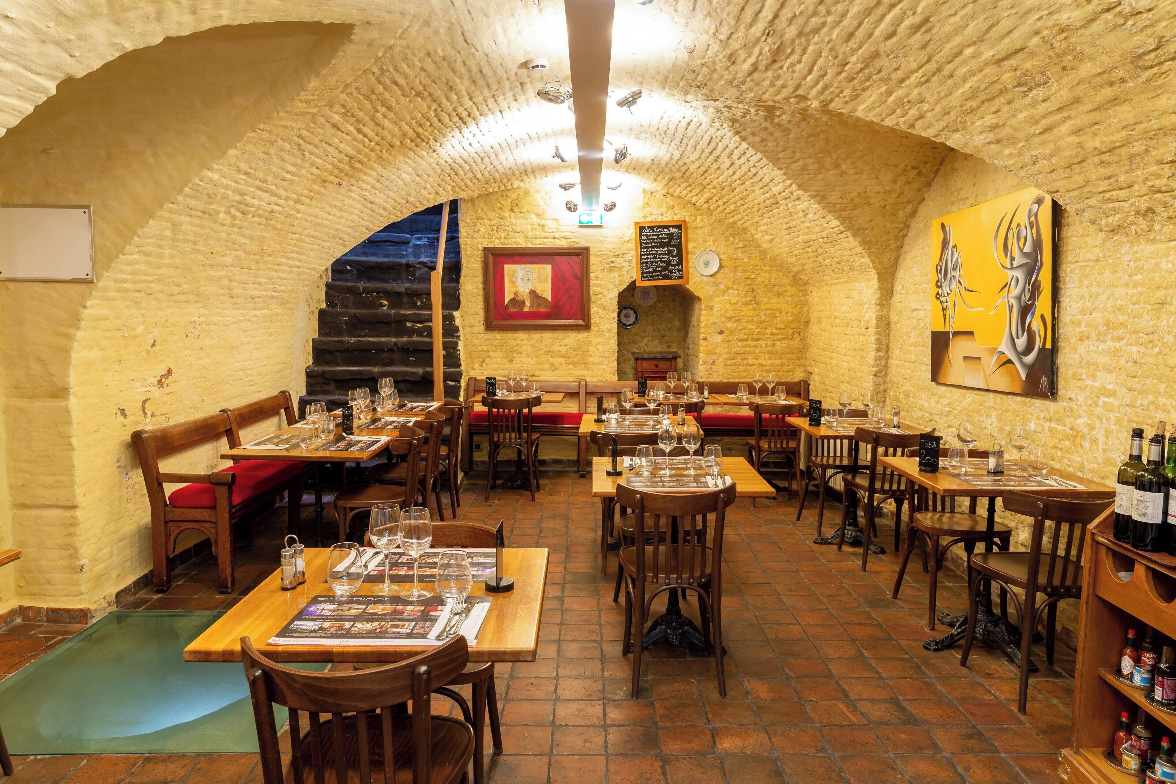 Een interieur met bakstenen muren, houten tafels en stoelen, met een wijnrek en een lijst met een afbeelding aan de muur.