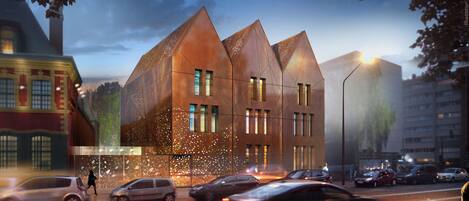 A modern building with a unique triangular roof design, large windows, and a street view with cars and pedestrians.