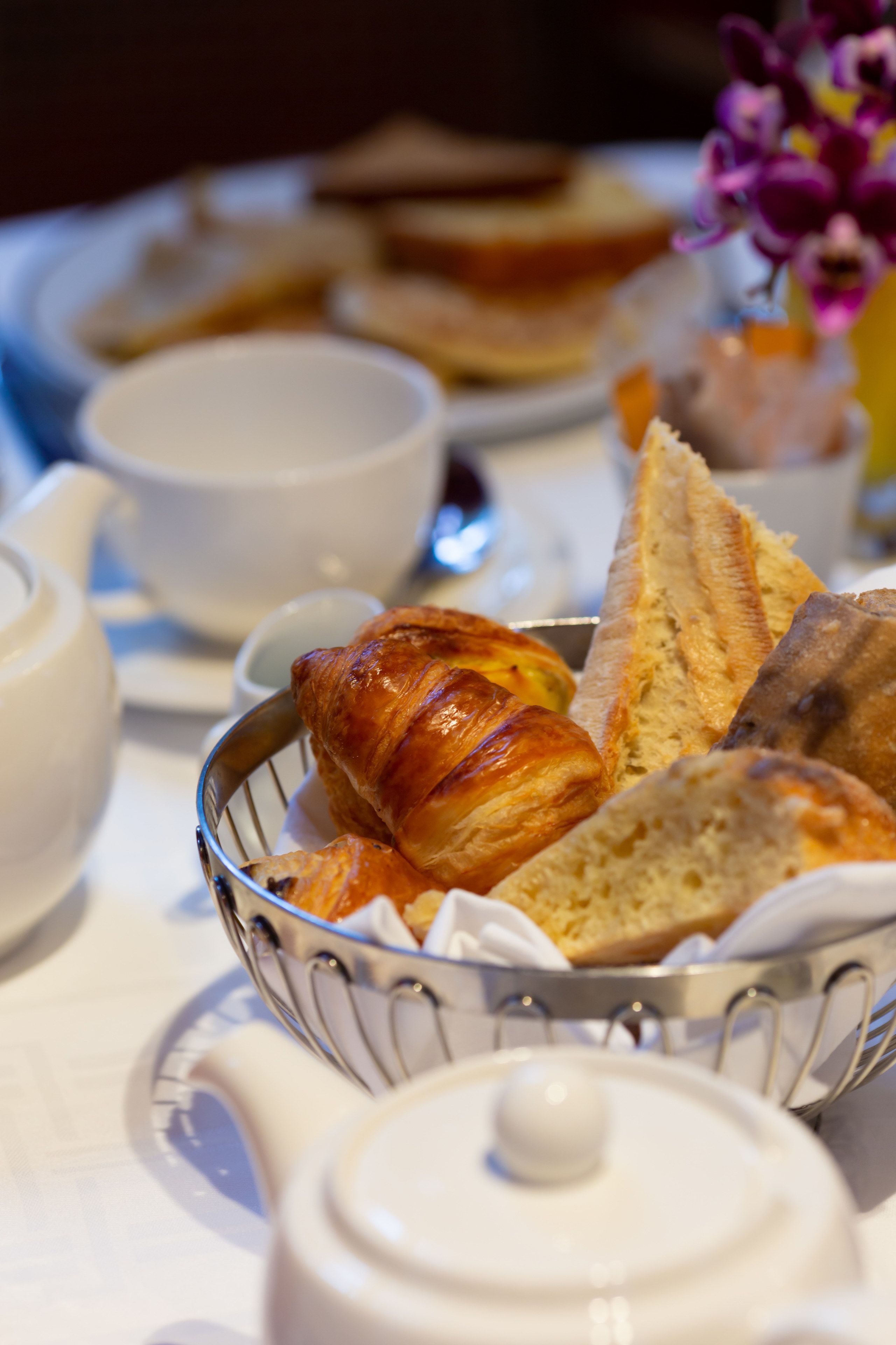 A breakfast setting with bread, croissants, and a teapot on a table.