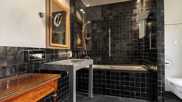 Une salle de bain moderne avec un mur recouvert de carreaux noirs, un meuble-lavabo en bois, un lavabo en verre, une baignoire et un espace douche.