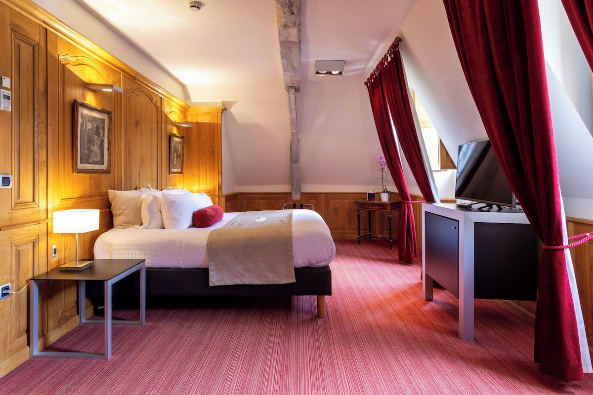 Une chambre d’hôtel comprenant un lit, une table de chevet, une lampe et un bureau avec une télévision.