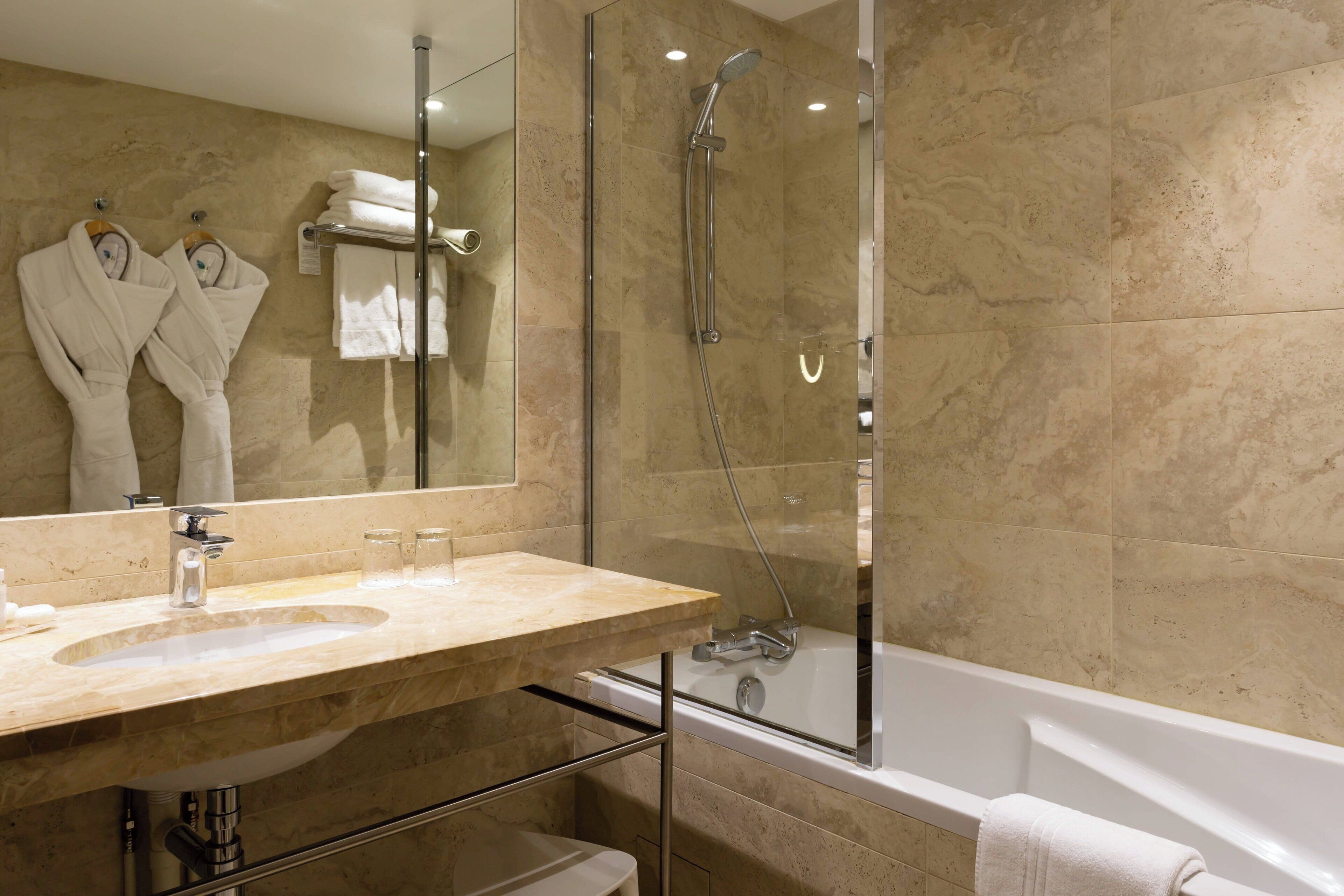 Un baño moderno con lavamanos de mármol, ducha con mampara de vidrio y bañera.