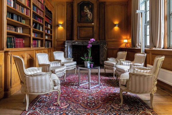 A library with wicker chairs, a patterned rug, and bookshelves.