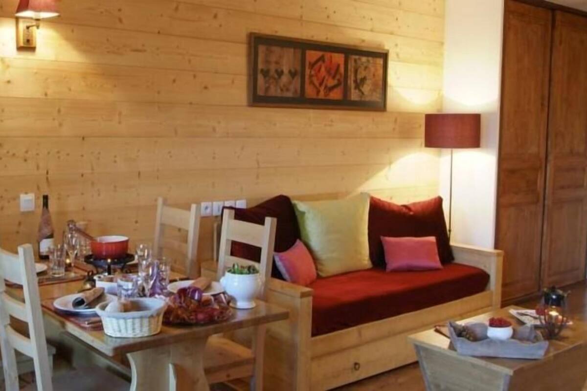 A wooden interior with a dining table, chairs, a sofa, and a lamp.