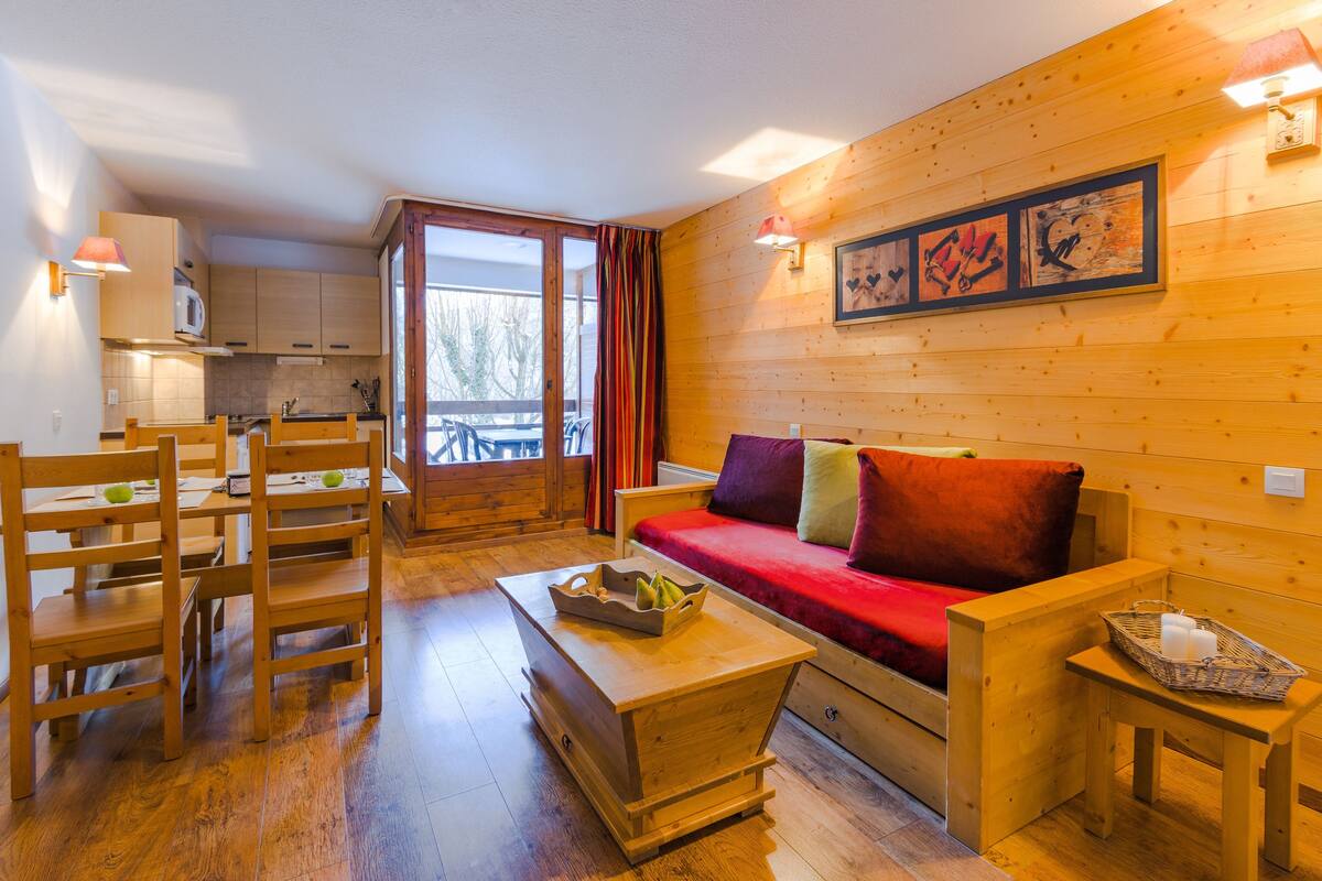 A wooden interior with a sofa, wooden chairs, a small table, and a kitchen area.
