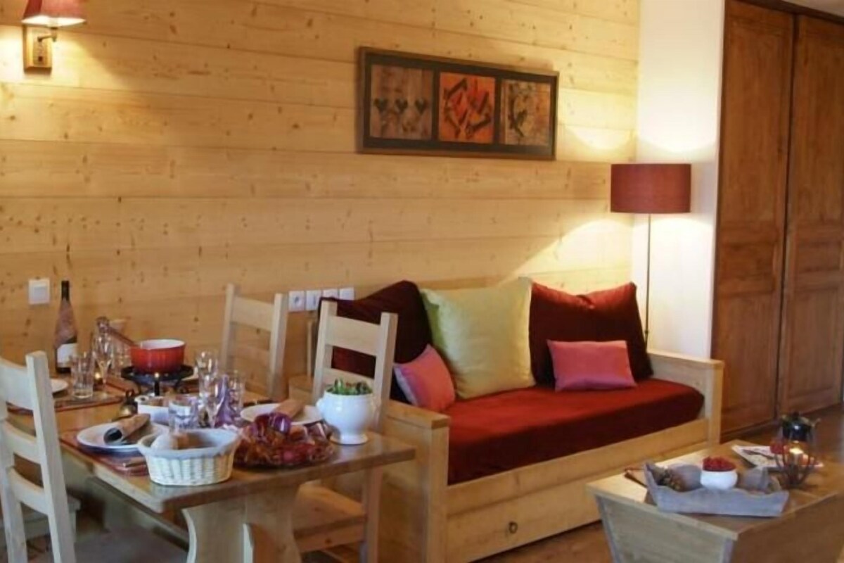 A wooden interior with a dining table, chairs, a sofa, and a lamp.
