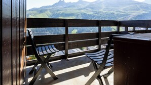 Un balcon avec une balustrade en bois, deux chaises à rayures et une table.