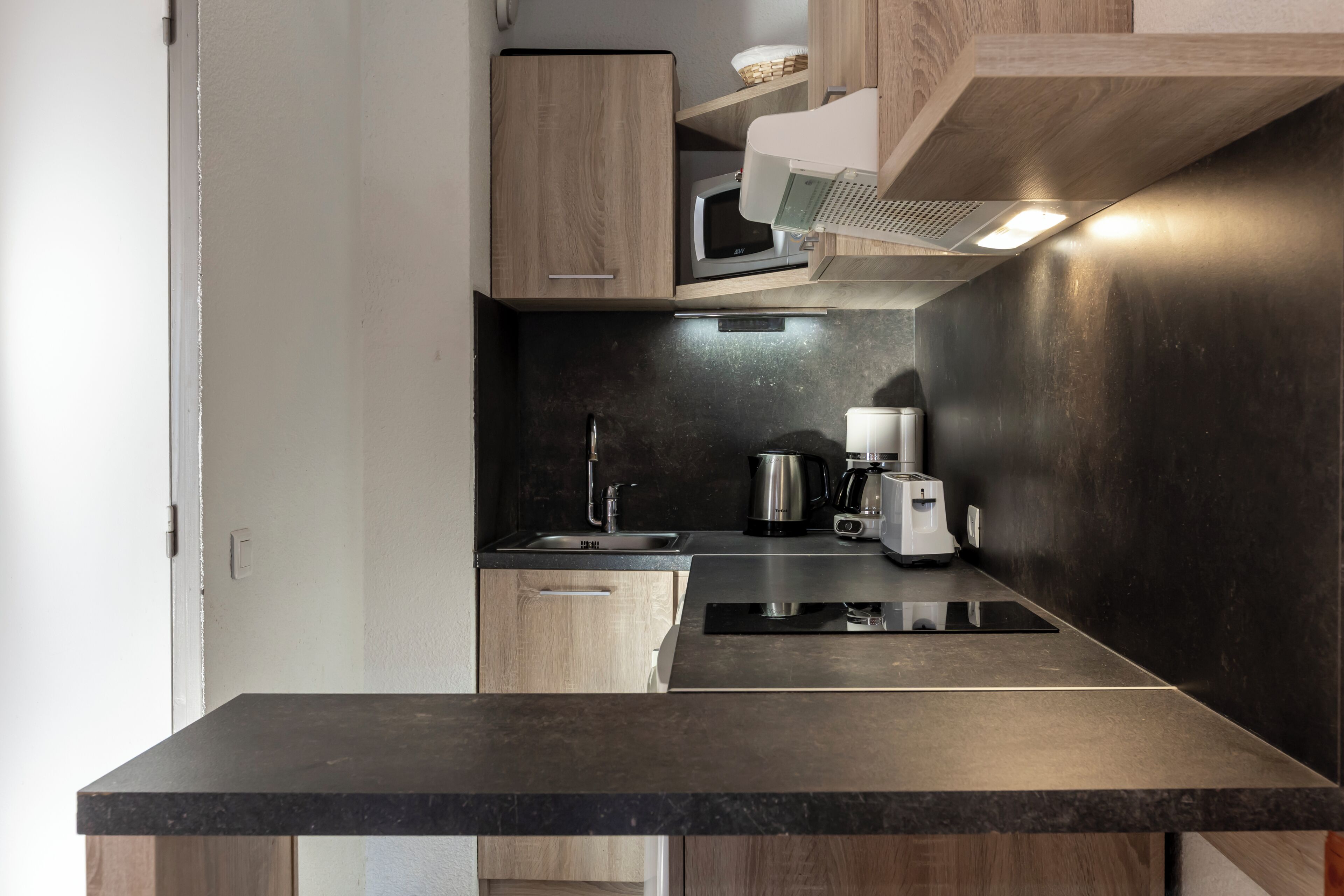 A modern kitchen with a dark countertop, stainless steel appliances, and wooden cabinetry.