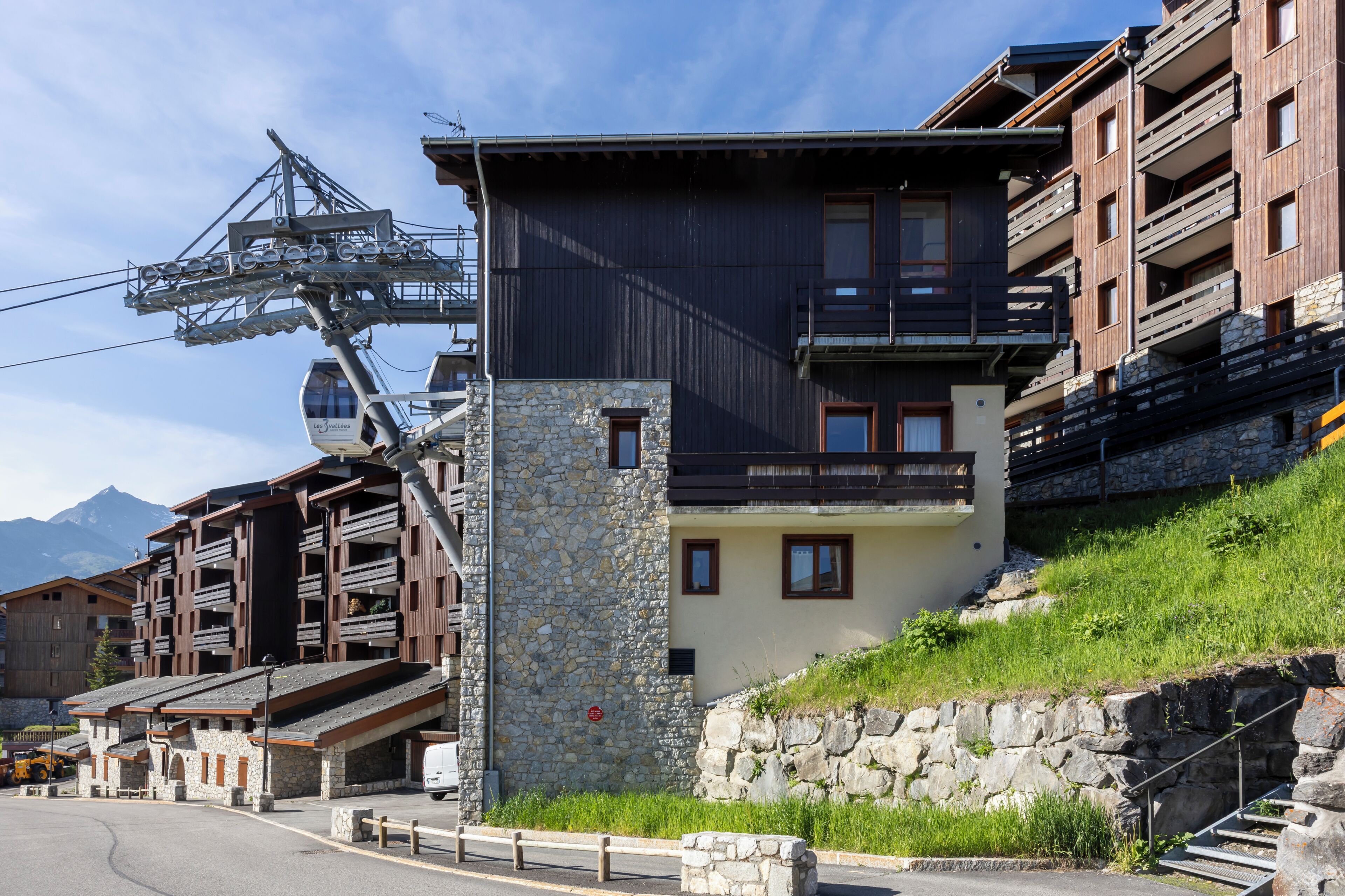 Un albergue de montaña con fachada de piedra, balcones de madera y un telesilla al fondo.