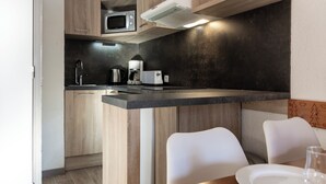 Une cuisine moderne avec des meubles en bois, un four à micro-ondes, une machine à café et un coin repas avec des chaises blanches.