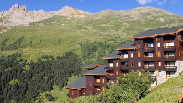 Un immeuble à plusieurs étages, doté de balcons, qui se dresse sur fond de montagnes.