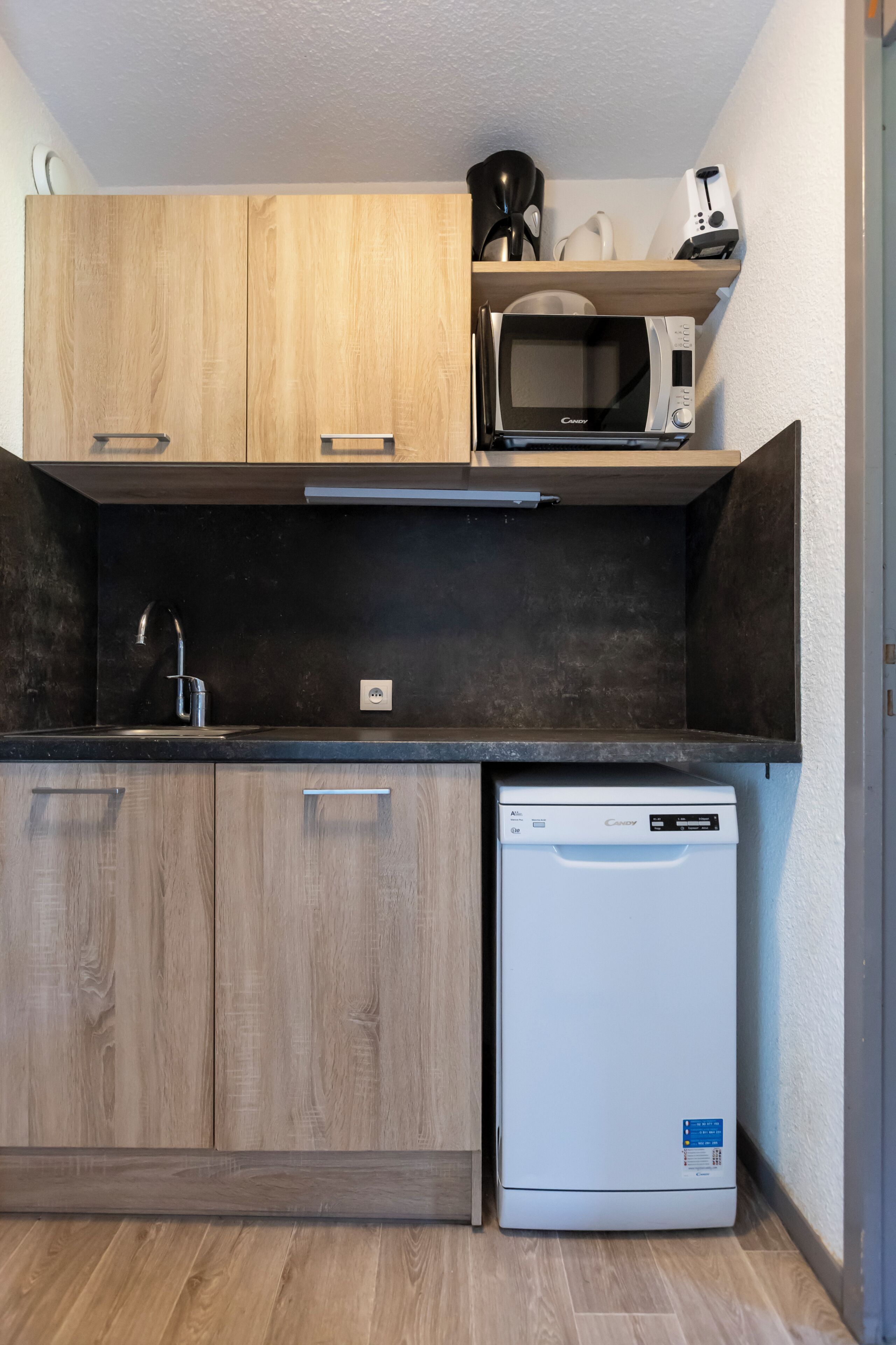 Een kleine keuken met houten kastjes, een magnetron, een koffiezetapparaat en een vaatwasser.