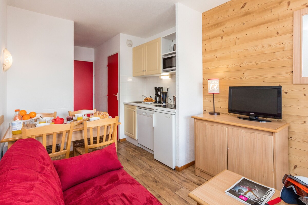 A compact living space with a kitchenette, a dining area, and a seating area with red cushions.