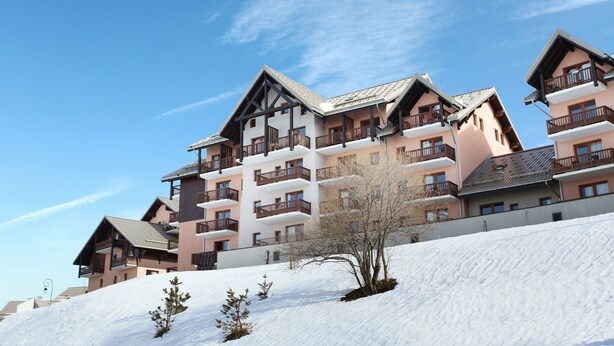 A multi-story hotel with balconies and a snow-covered slope. - Résidence Odalys Les Lumières de Neige (Valmeinier)