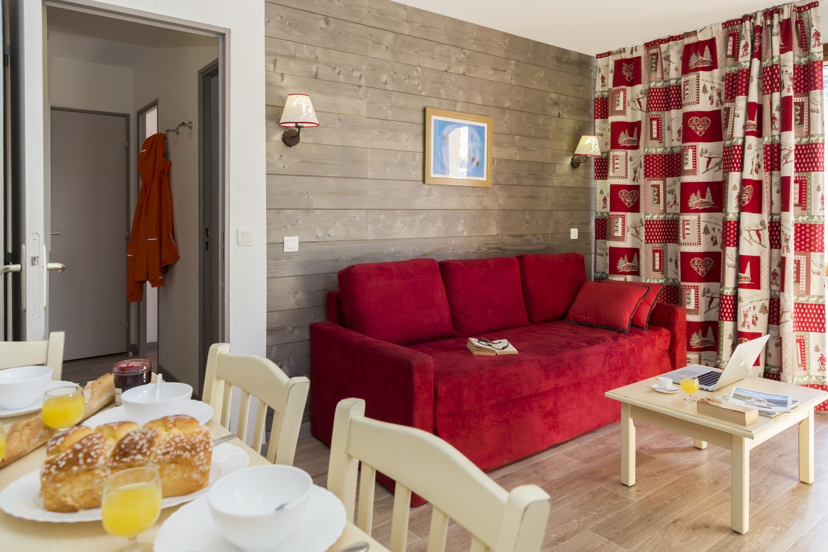 Een woonkamer met een rode bank, een houten wand en een tafel met ontbijtartikelen.
