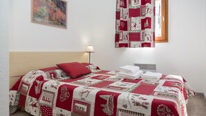 A neatly made bed with a red and white quilt, a red pillow, and a folded white towel on the side. - Résidence Odalys Les Lumières de Neige (Valmeinier)