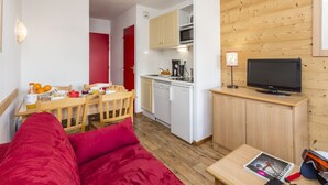 A compact living space with a kitchenette, a dining area, and a seating area with a red sofa. - Résidence Odalys Les Lumières de Neige (Valmeinier)