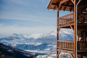 Une cabane en bois dotée d’un balcon donnant sur des montagnes enneigées.