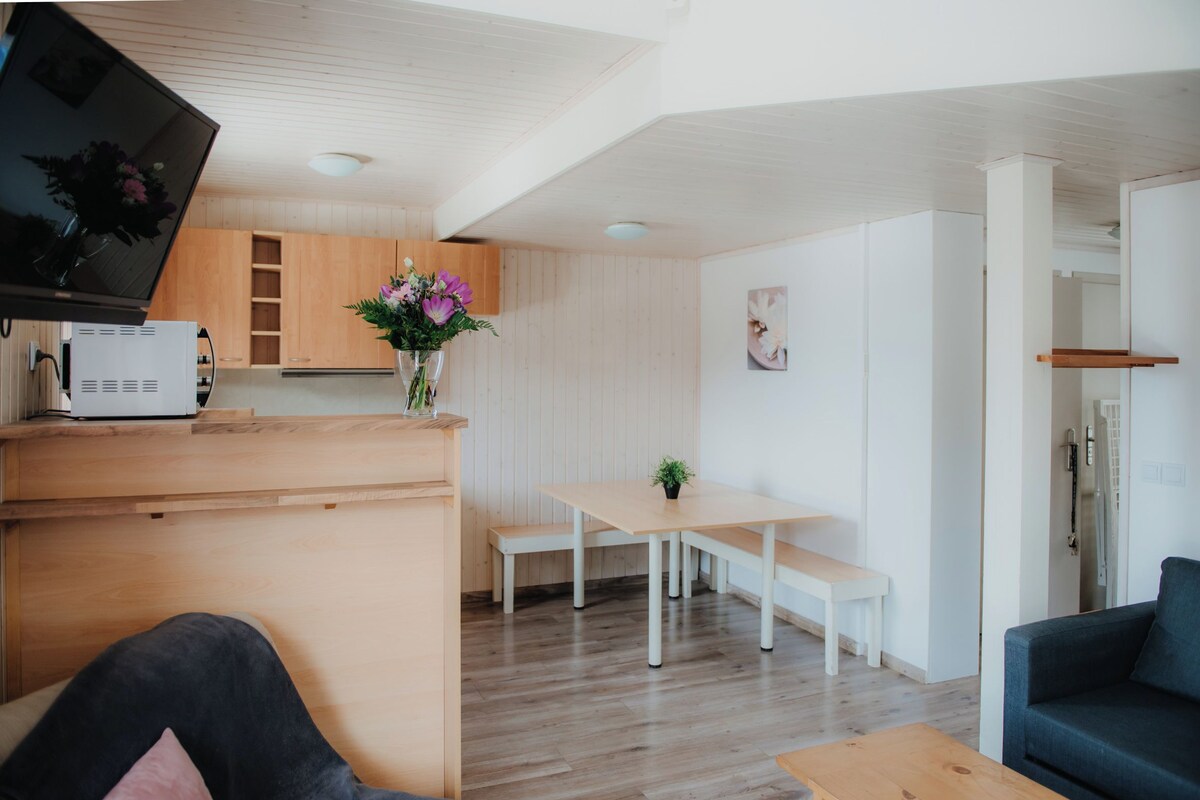 Una sala moderna con una mesa de centro de madera, un sofá azul y un comedor con una mesa blanca y bancos.