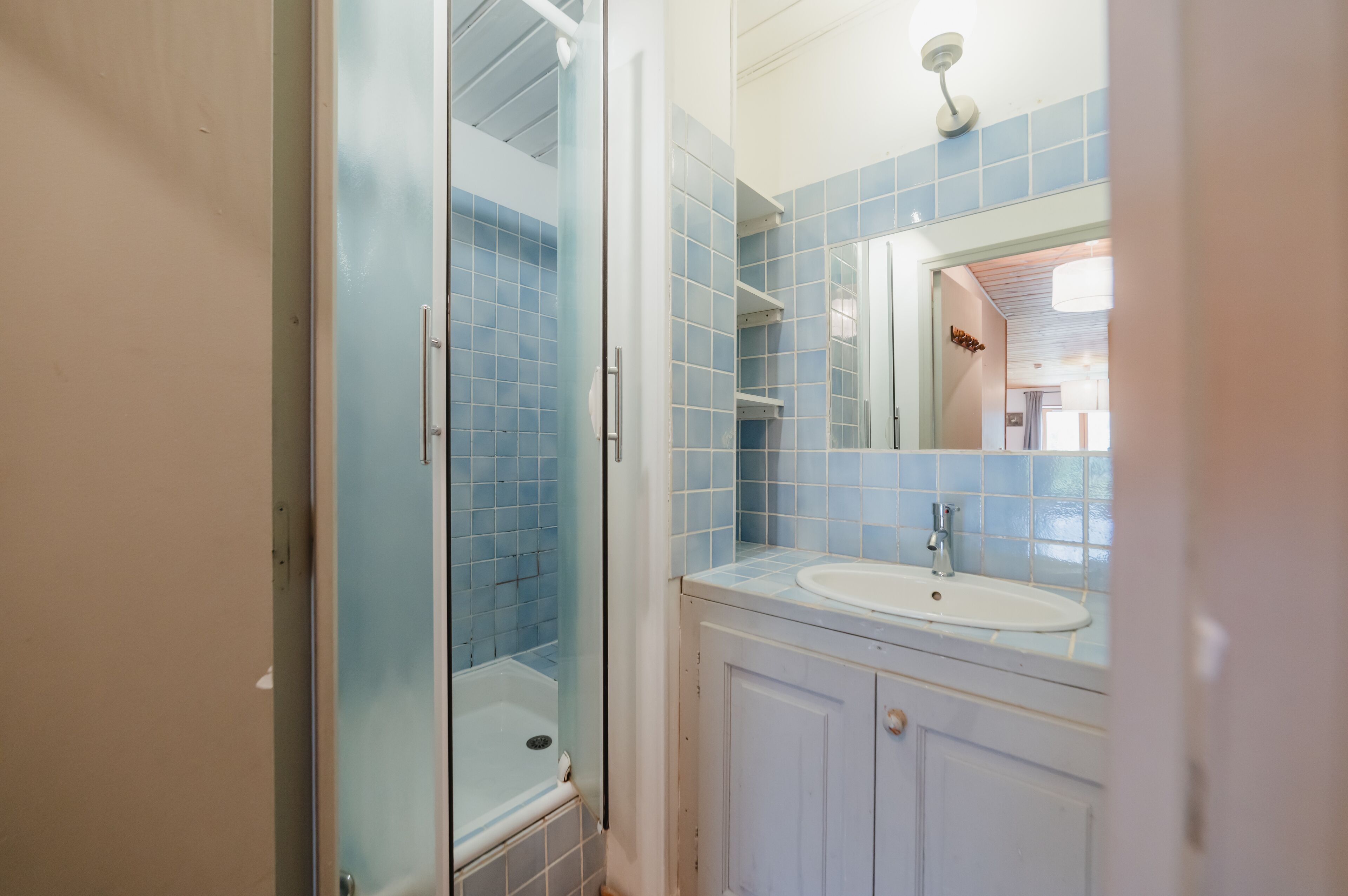 A bathroom with a glass shower enclosure, a sink, and a mirror.