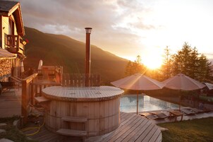Une terrasse en bois avec un jacuzzi, des chaises longues et des parasols.